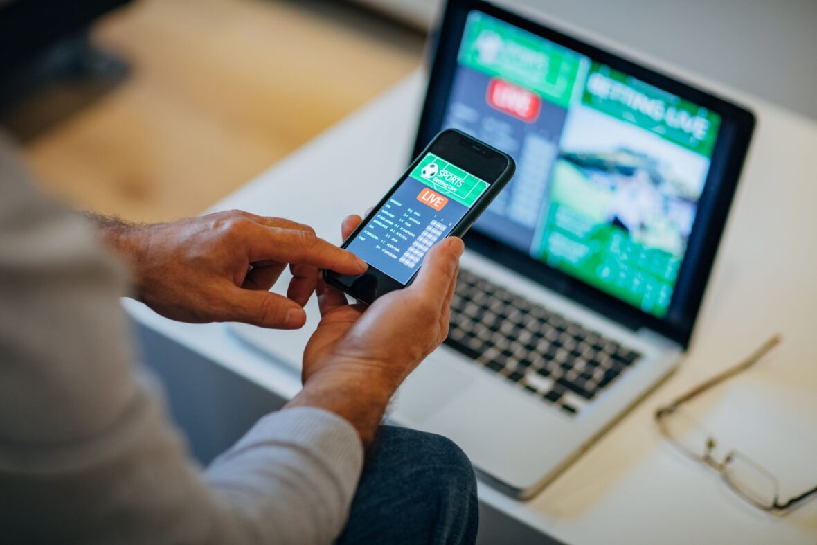 Picture of a man surfing a sports betting site in his mobile and laptop