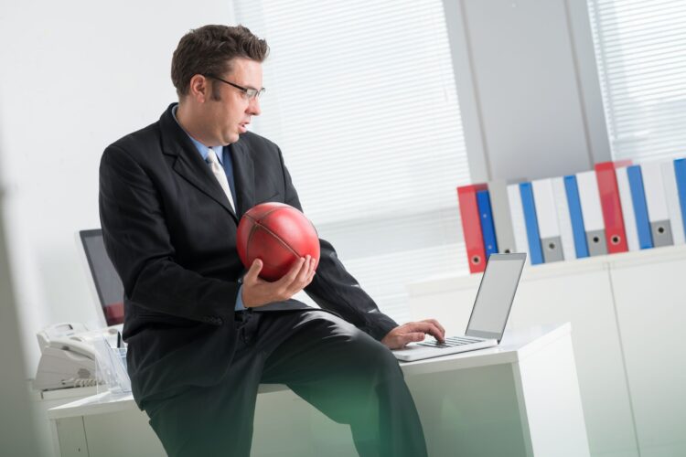 Picture of a man betting online using his laptop while holding a football